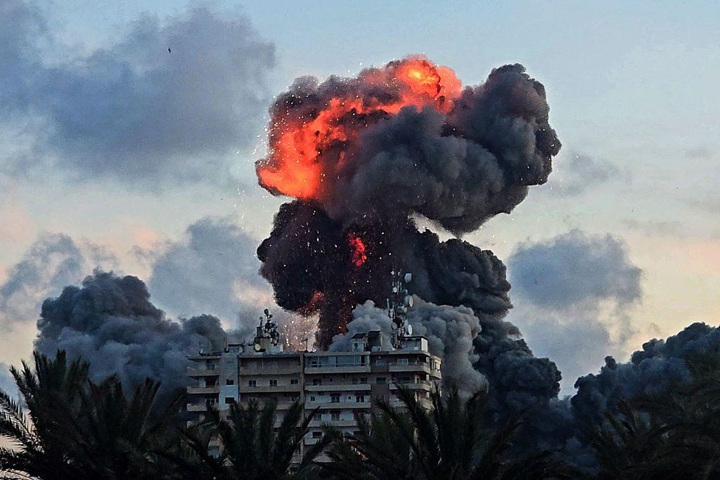 كرة نارية ودخان يتصاعدات فوق مبنى في مدينة صور عقب غارة إسرائيلية، يحيط بالمبنى مجموعة من الأشجار. الصورة التقطت في الصباح الباكر.