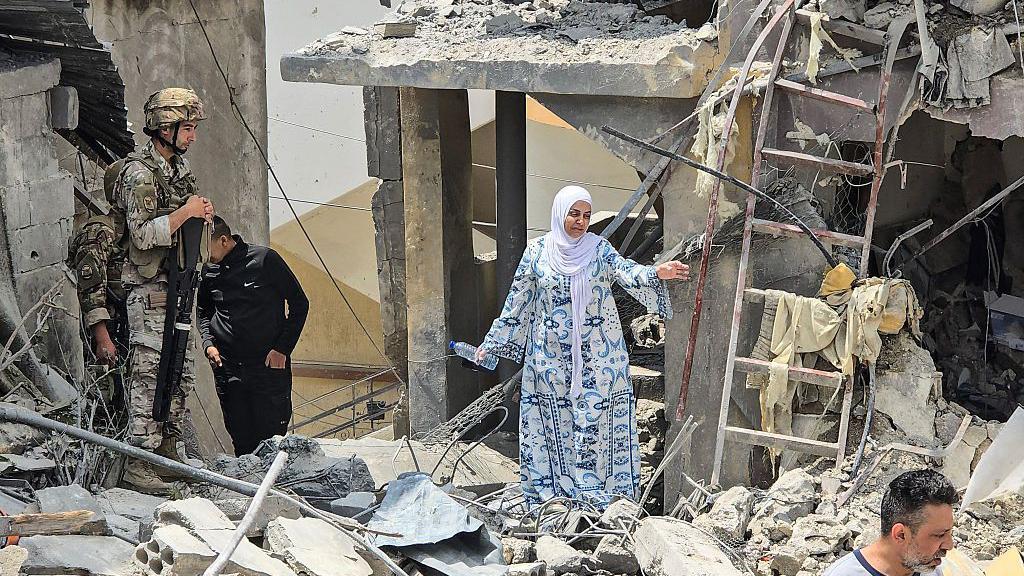 امرأة تشق طريقها عبر الأنقاض بينما ينظر جندي لبناني إلى موقع مبنى سكني دمر في غارة إسرائيلية في بلدة برج الشمالي الجنوبية، على مشارف مدينة صور، لبنان (27 مايو 2026).
